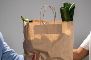 Hands holding out brown paper bag full of food